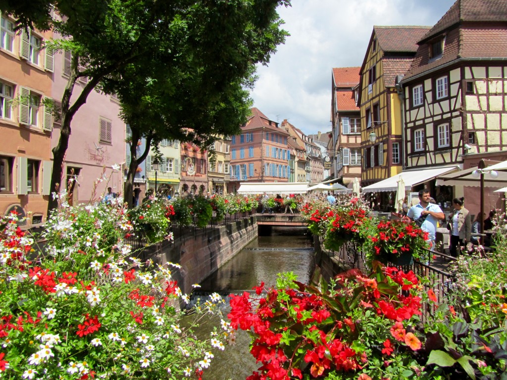 Beautiful flowers line the river next to colourful houses in Colmar, Alsace