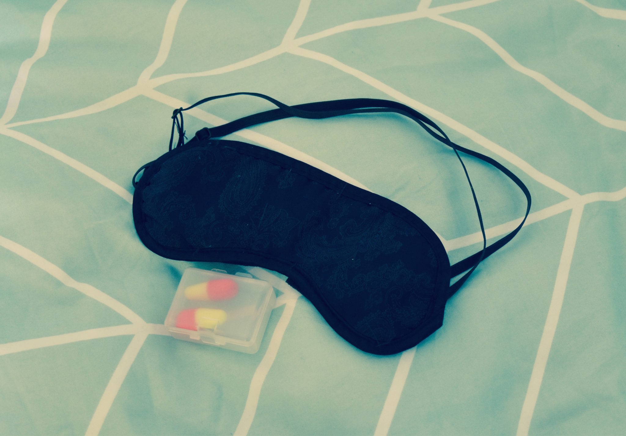 an eye mask and ear plugs on a green bed cover 