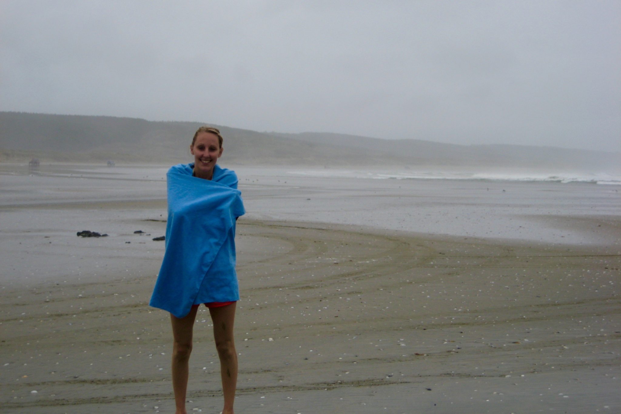Hayley wrapped in a blue travel town on a misty beach in New Zealand 