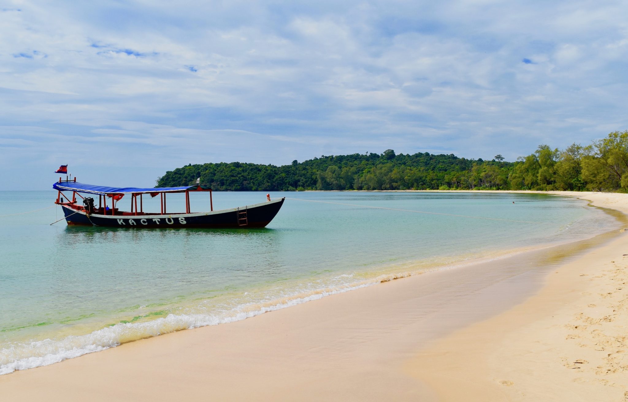 A traditional Cambodian boat moored at a white sand beach 