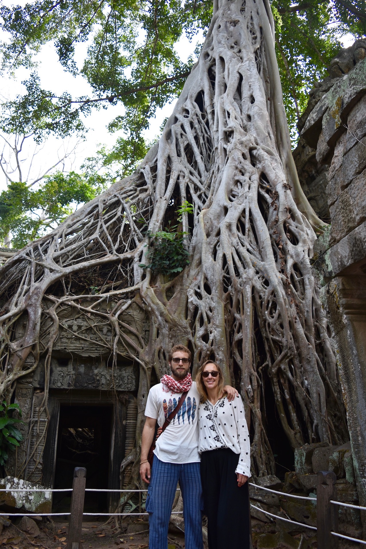 Hayley and Enrico stood in front of part of a tree covered temple - Ta Prohm